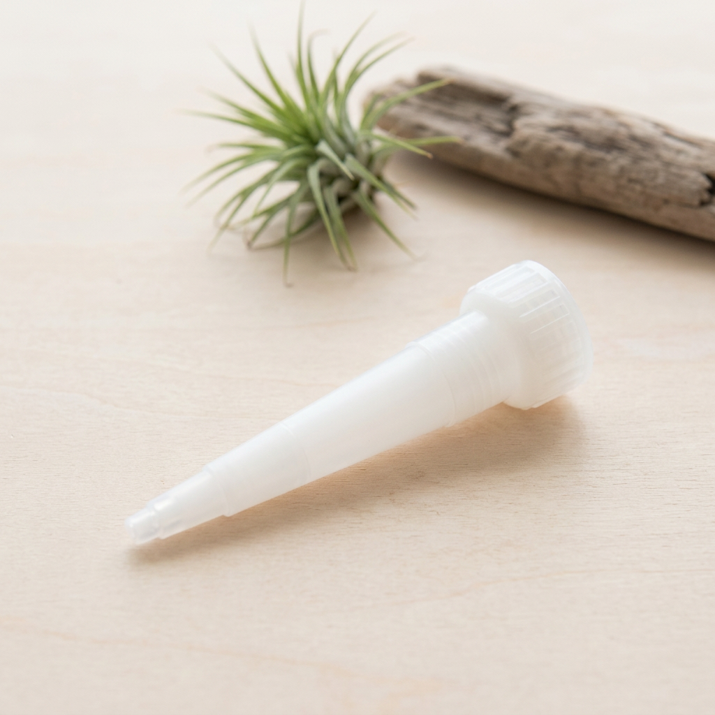 Large-tube Snip Tip applicator styled beside an air plant and driftwood; plant, adhesive and mounting materials not included.